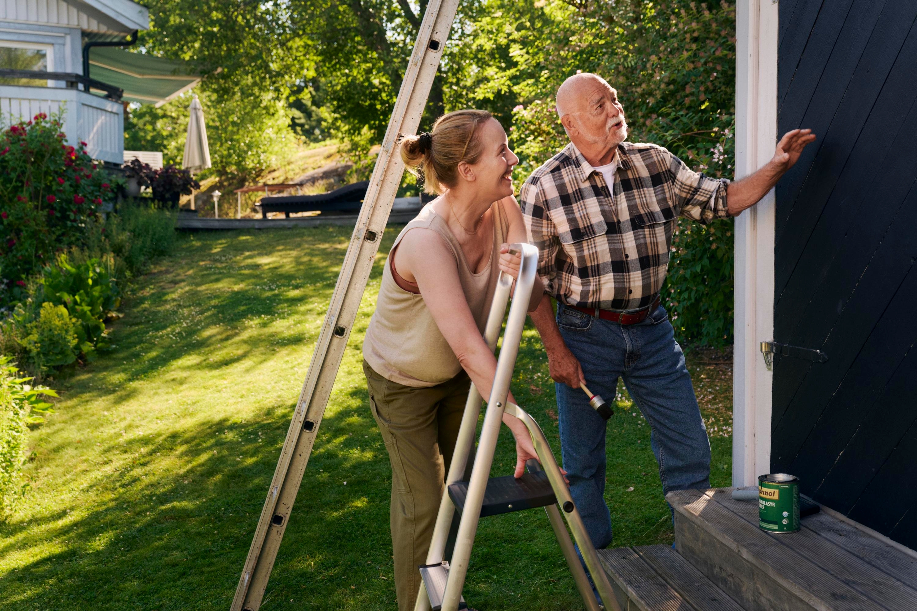 En kvinna och en äldre man målar ett hus