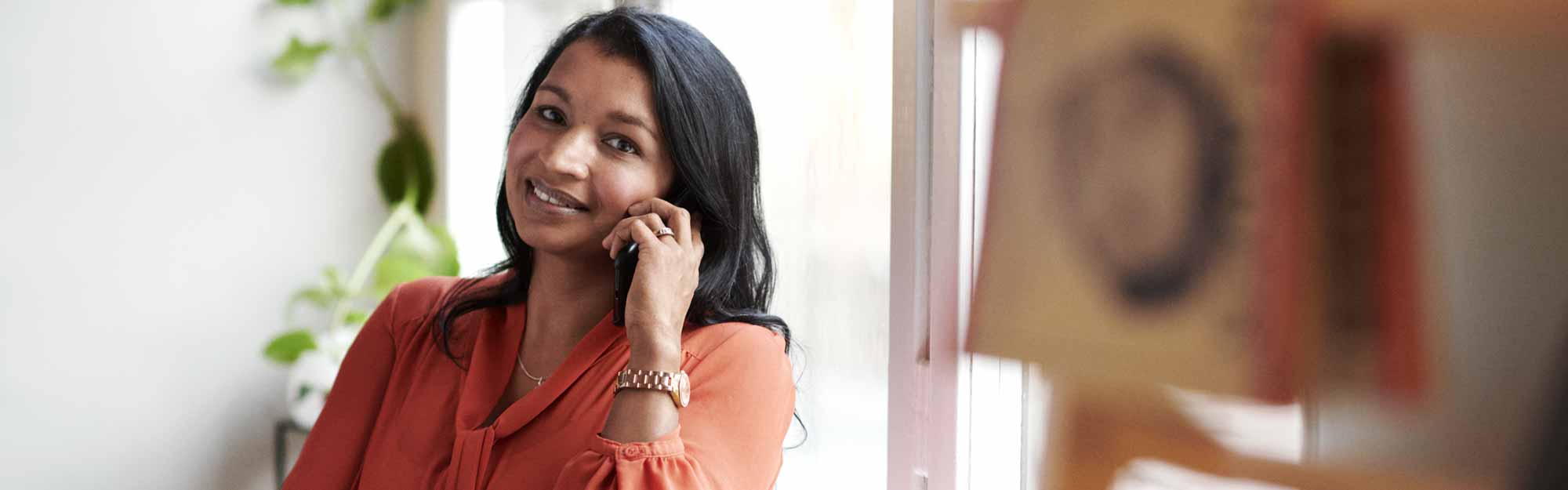 Leende affärskvinnan med orange blus talar i mobil