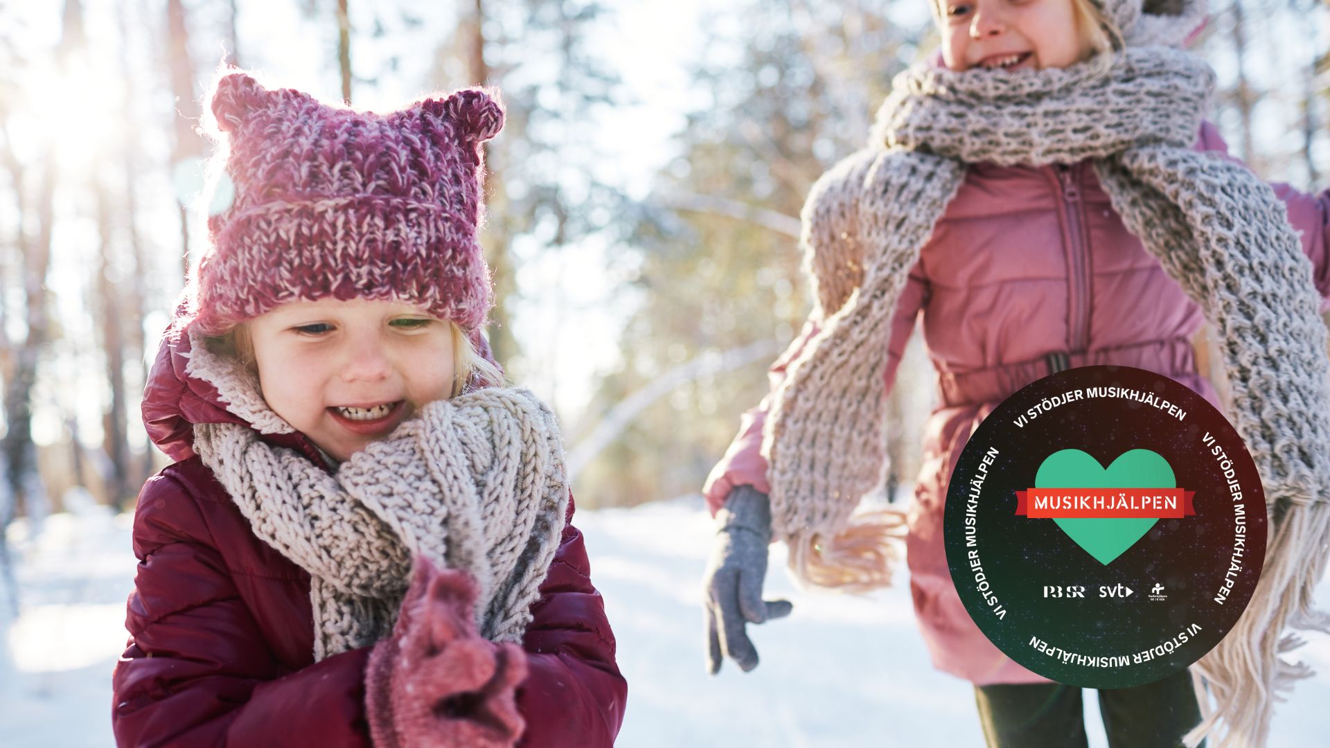 Två barn leker i snön. Musikhjälpens logo i bilden till höger. 